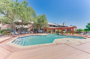 A large outdoor swimming pool with a wooden deck and a building in the background.